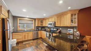A modern kitchen with wooden cabinets, a stainless steel refrigerator, a built-in oven, and a granite countertop. - Lies by Avantstay Indoor Heated Pool + Game Lounge Pool Table + Foosball (North Creek)