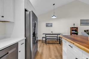 Eine moderne Küche mit Edelstahlkühlschrank, Holztisch und einer Pendelleuchte.