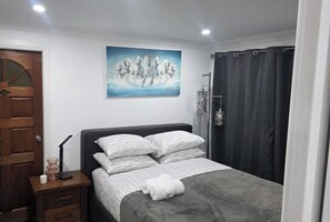 A bedroom with a bed, a wooden door, a painting, a bedside table, and a shower curtain.