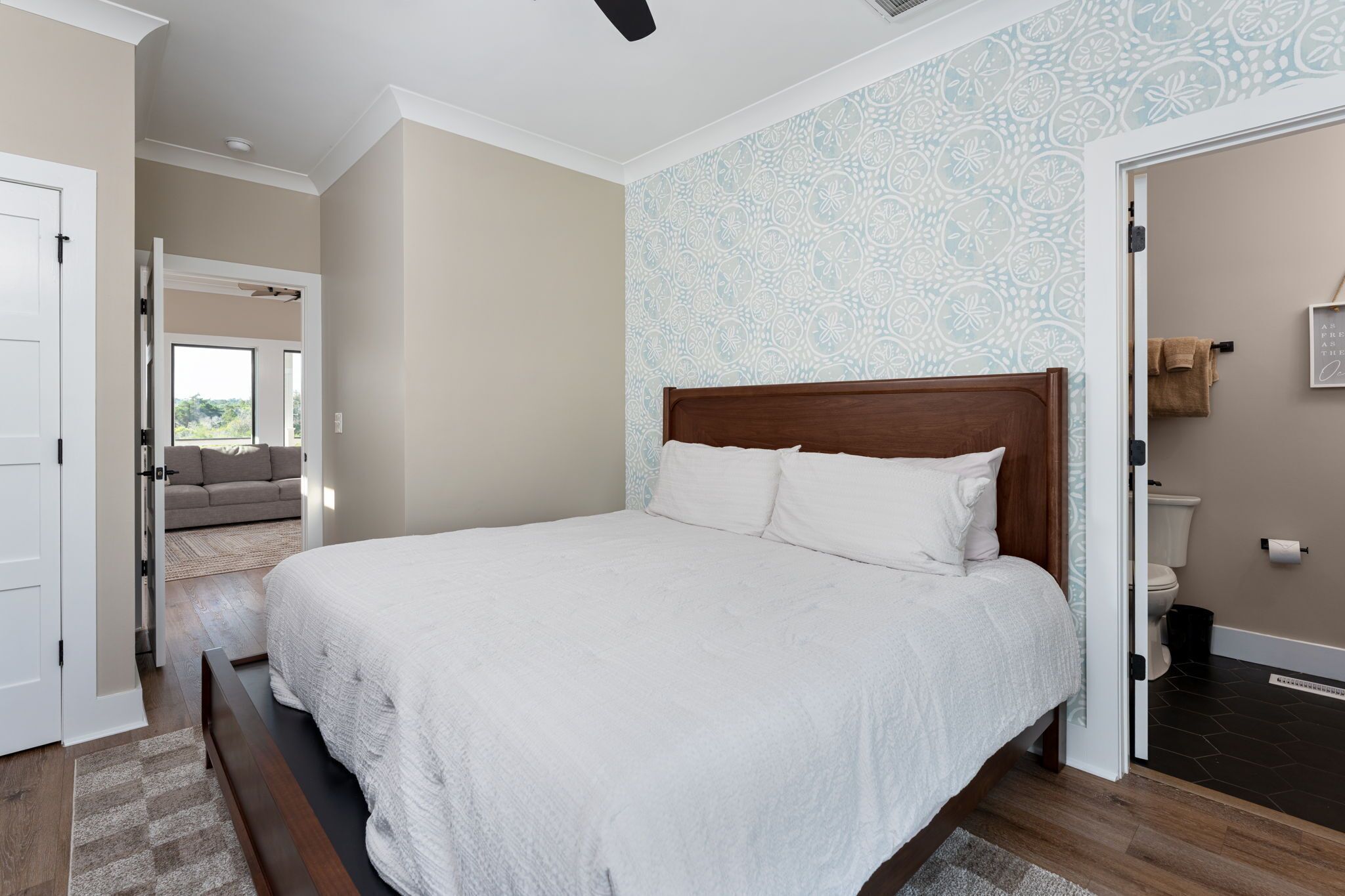 Un dormitorio con una cama grande, vista a un área de estar y un baño con inodoro y lavamanos.
