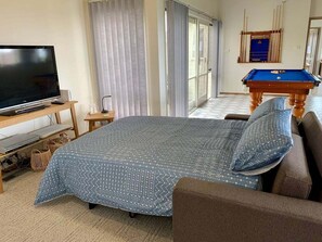 A bedroom with a bed, a television, a pool table, and a window with curtains. - Cue the Views at Seven (Clifton Springs)