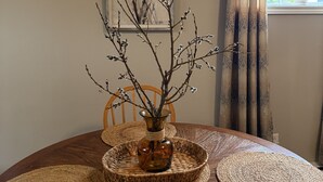 Una mesa de comedor con un florero de ramas, una silla y individuales tejidos.