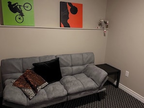 Ein graues Sofa mit schwarzen und gemusterten Kissen, ein kleiner schwarzer Beistelltisch und ein Kunstwerk an der Wand.