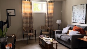 Una sala de estar con sofá, dos sillones, una mesa de centro, una lámpara, un cuadro y un ventanal con cortinas.