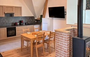 Una cocina con zona de comedor, un televisor montado en la pared y una estufa de leña.