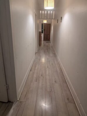 Ein Flur mit Holzboden, weißen Wänden und einer Tür am Ende.