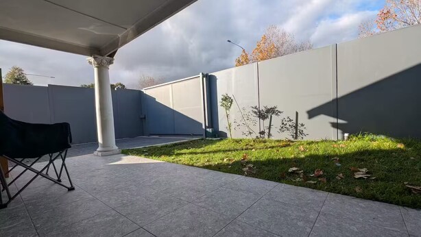 Een overdekt terras met betegelde vloer, een witte kolom en een zwarte klapstoel.