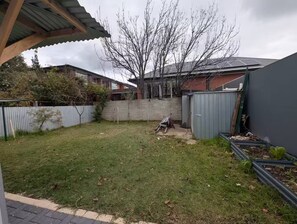 Ein Garten mit Rasenfläche, einer Betonmauer, einem Metallschuppen und einem Baum.