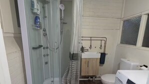 Een badkamer met een douchecabine van glas, toilet, wasmachine en een wastafel met spiegel.