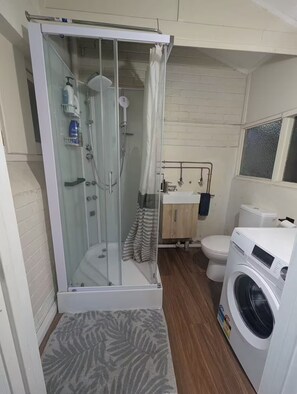 Ein Badezimmer mit Duschkabine, Toilette, Waschmaschine und Waschbecken mit Spiegel.