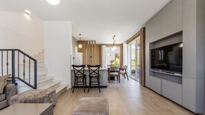 Eine moderne Küche mit einem großen Fernseher, ein Essbereich mit Stühlen und eine Treppe, die zu einer weiteren Ebene führt.