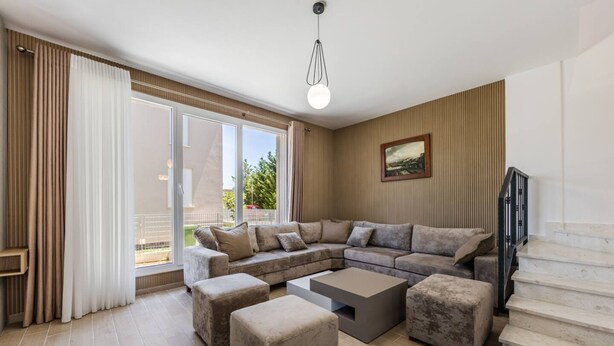 Ein modernes Wohnzimmer mit einem Ecksofa, Poufs, einem Couchtisch und einer Treppe.