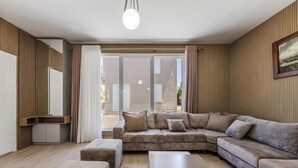 Ein modernes Wohnzimmer mit einer Eckcouch, einem Flachbildfernseher und einem großen Fenster mit Vorhängen.