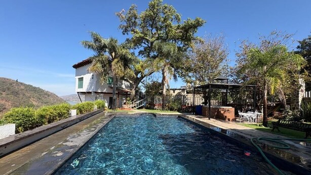 Una piscina de agua cristalina, rodeada de vegetación y un edificio con tejado rojo.