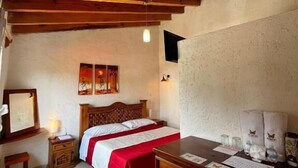 Un dormitorio con techo de madera, una cama con colcha roja, una mesita de noche con lámpara y un aparador.