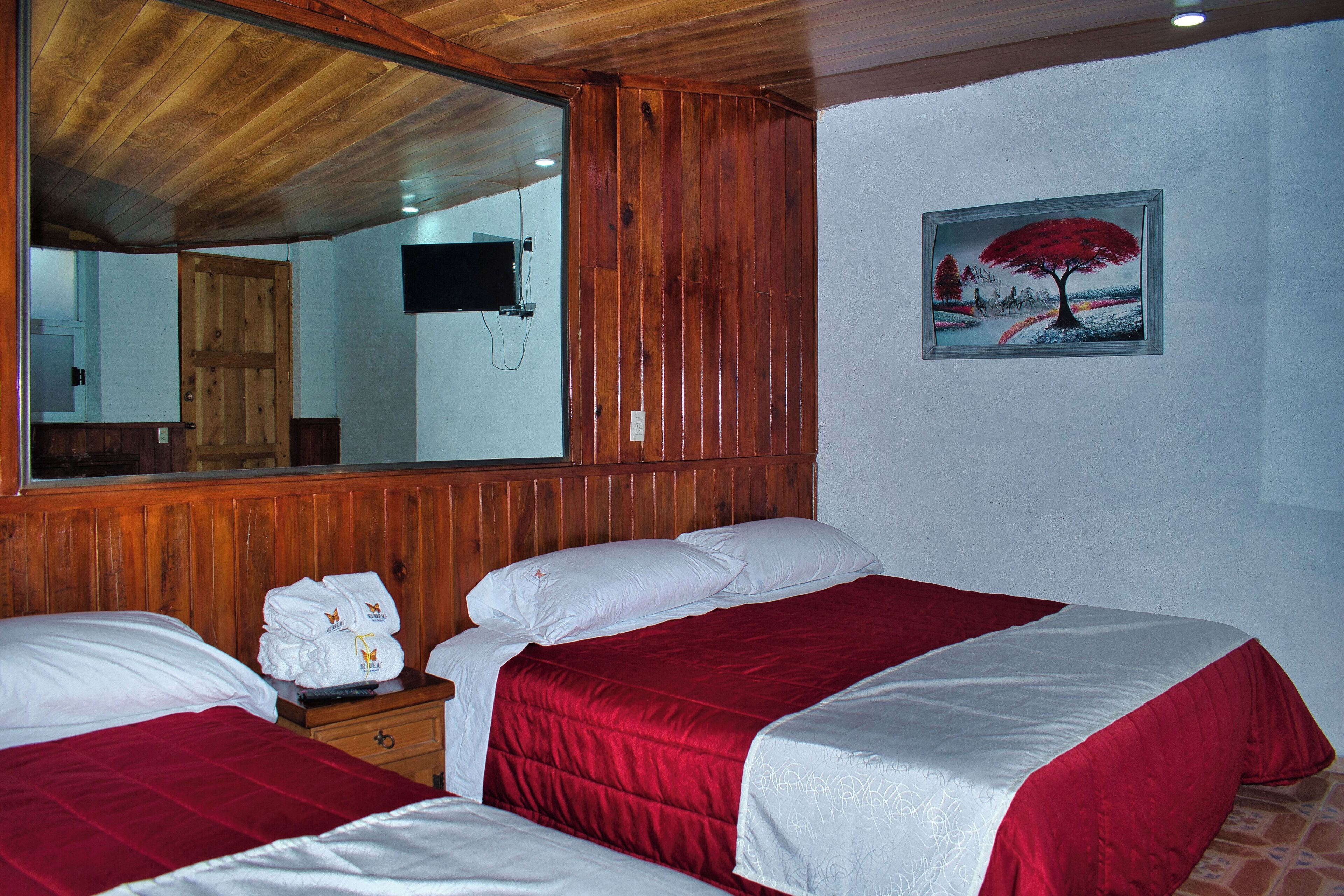 Ein Hotelzimmer mit zwei Betten, Holzvertäfelung, einem großen Spiegel und einem Baumgemälde.