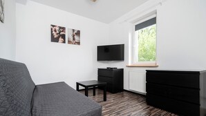 Une chambre moderne avec un canapé gris, un téléviseur à écran plat, une petite table et une commode.