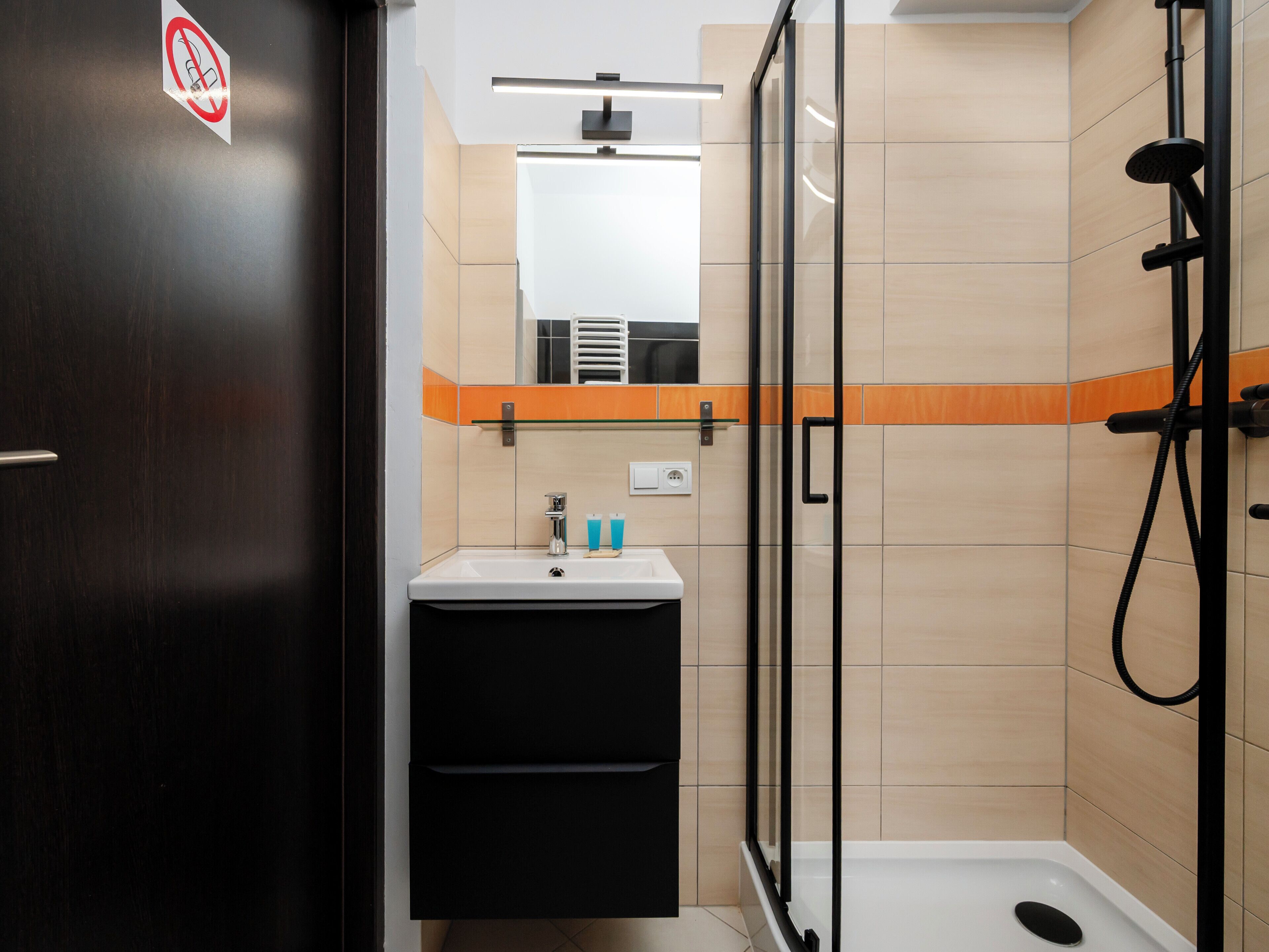 A modern bathroom with a glass shower enclosure, a sink with a mirror, and a dark wooden door.