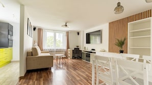 A modern kitchen with a dining area, wooden flooring, and a TV mounted on the wall. - Gdynia Marina Harmony Apartment (Gdynia)