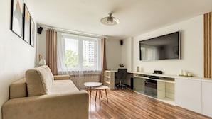 A modern living room with a sofa, a dining table, a kitchen area, and a large TV mounted on the wall. - Gdynia Marina Harmony Apartment (Gdynia)