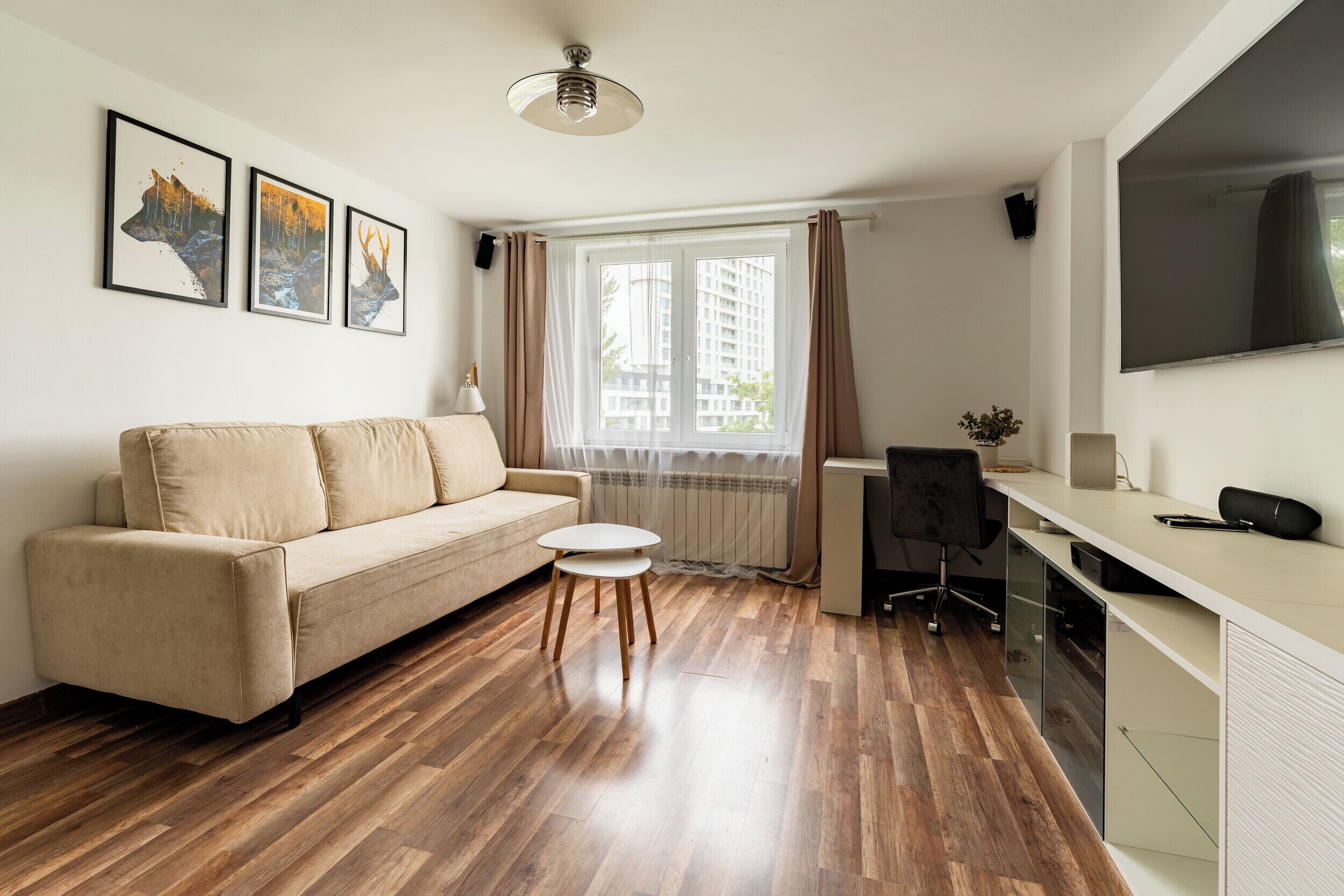 A modern living room with a sofa, a small round table, a desk with a chair, and a large TV.