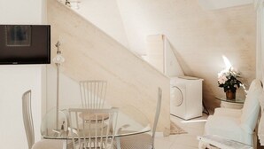 Un espacio habitable moderno con una mesa de vidrio, sillas blancas, un sofá, un televisor montado en la pared y una escalera.