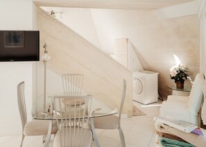 Ein moderner Wohnraum mit einem Glastisch, weißen Stühlen, einer Couch, einem an der Wand befestigten Fernseher und einer Treppe.