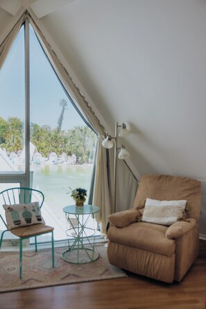 Ein Zimmer mit großem Fenster, einem braunen Sessel, einem kleinen runden Tisch und einem grünen Stuhl.