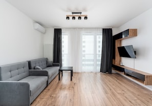 Una sala de estar moderna con un sofá gris, una mesita, un televisor en un estante de madera y una lámpara en el techo.
