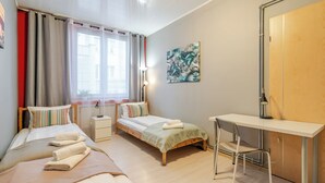Ein Schlafzimmer mit zwei Betten, einem Schreibtisch, einem Stuhl und einem Fenster mit Vorhängen.