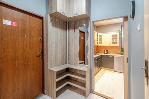 A hotel room with a wooden door, a mirror, a built-in bench, and a view into the kitchen area. - Matejki Central Apartment (Katowice)