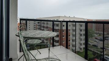 En balkon med et rundt bord og stole, gelænder i metal og udsigt til bygninger i baggrunden.