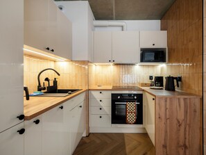 Eine kleine Küche mit weißen Schränken, einer Holz Arbeitsplatte, einem eingebauten Ofen und einer Mikrowelle.