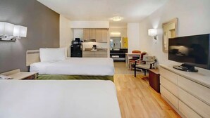 Ein Hotelzimmer mit zwei Betten, einem Fernseher, einem Schreibtisch und einer Küchenzeile.