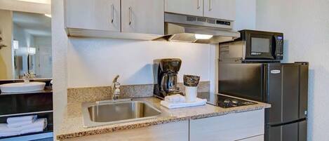 A kitchen with a stainless steel sink, a coffee maker, a microwave, and a refrigerator.