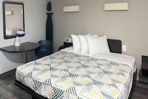 Quarto de hotel com cama, escrivaninha, cadeira, espelho e mesa de cabeceira.