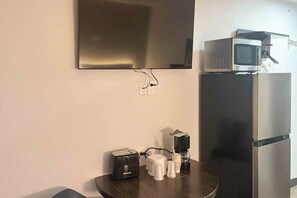 Una kitchenette con microondas, tostadora y cafetera sobre una mesa de madera, un refrigerador y un televisor de pantalla plana montado en la pared.
