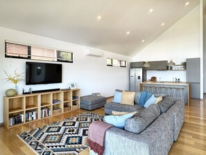Un salon moderne doté d’un téléviseur à écran plat, d’un canapé, d’un tapis à motifs et d’un coin cuisine avec un réfrigérateur et des tabourets de bar.
