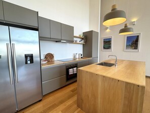 Une cuisine moderne dotée d’appareils électroménagers en acier inoxydable, d’un plan de travail en bois et de luminaires suspendus.