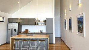 Una cucina moderna con isola centrale, sgabelli da bar, frigorifero e illuminazione a sospensione.