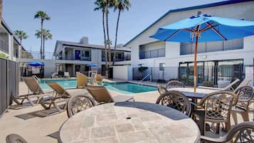 A poolside area with lounge chairs, a table, and umbrellas.