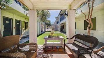 Un espacio exterior cubierto con mobiliario de mimbre, una mesa con flores y vista al interior del edificio.