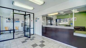 Zona de recepción con mostrador de check-in, puertas de cristal y suelo de baldosas.