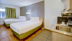 Ein Hotelzimmer mit zwei Betten, einer Küchenzeile, einem Fenster mit Vorhängen und einer Wandleuchte.