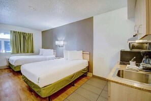 Hotelkamer met twee bedden, een kitchenette, een raam met gordijnen en een wandlamp.
