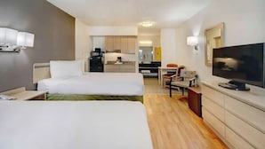 Habitación de hotel con dos camas, televisión, escritorio y kitchenette.