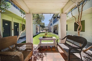 A covered outdoor area with wicker furniture, a table with flowers, and a view of the building's interior. - Cactus Country Retreat w/ Free Parking+Pool | 4.3 mi to Reid Park Zoo | 2 Units (Tucson)