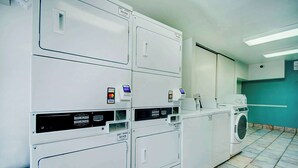 Un cuarto de lavandería con varias lavadoras y secadoras, un panel de control y piso de baldosas.