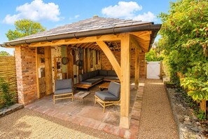 A covered outdoor seating area with a wooden pergola, a built-in bench, and a small table. - Stonethwaite Barn, Dalston -  a luxurious, dog friendly barn (Dalston)