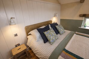 A bedroom with a wooden headboard, striped bedding, and decorative pillows. There is a bedside table with a lamp and a window with a view. - Stonethwaite Barn, Dalston - a luxurious, dog friendly barn (Dalston)